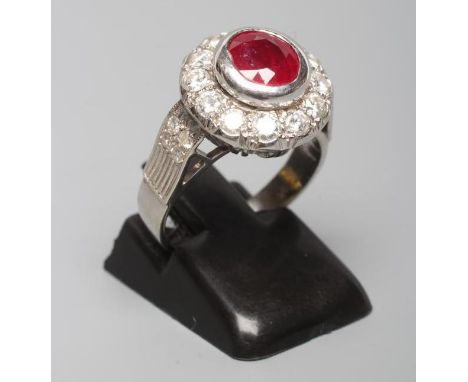 A RUBY AND DIAMOND CLUSTER RING, the circular facet cut ruby collet set to a border to twelve brilliant cut diamonds point se