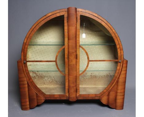AN ART DECO WALNUT DISPLAY CABINET of circular form with two astragal glazed doors with turned brass handles enclosing glass 