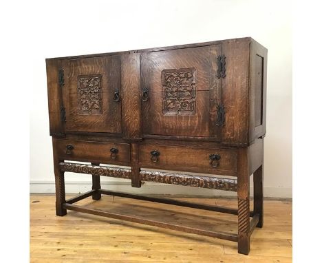 An Arts &amp; Crafts style oak sideboard, c.1920s, the rectangular caddy top above a pair of cupboard doors carved with folia