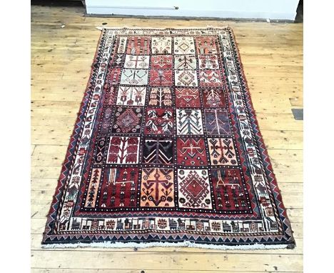 A hand woven tile pattern carpet, each tile decorated with stylised patterns in madder, ivory and indigo, within multiple ser