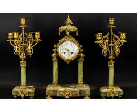 A French Green Onyx Clock Garniture comprising central portico clock, ormolu mounted, with white enamel dial and Arabic numer