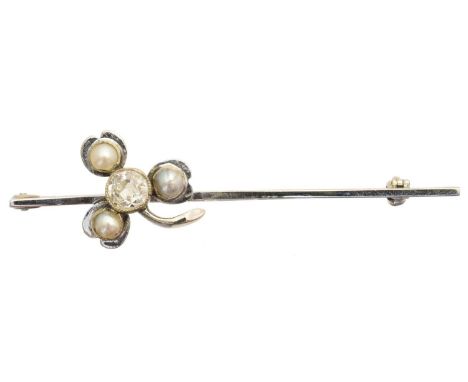 An early 20th century diamond and split pearl bar brooch, the old cut diamond and split pearl set shamrock atop the polished 