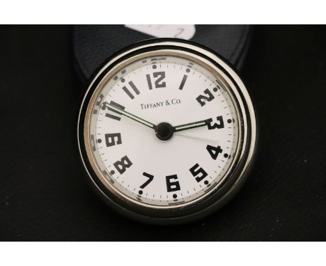 A chrome plated travel clock, white dial with black Arabic numerals, in leather case