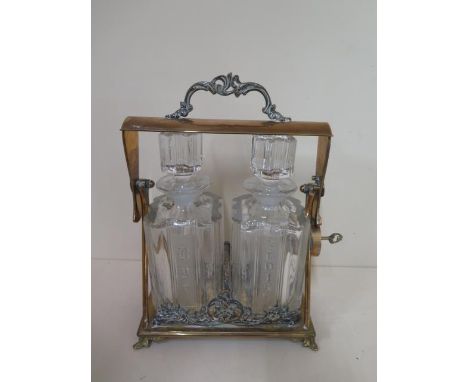 A brass two bottle tantalus Scotch and Rye, 32cm tall x 23cm wide, scotch decanter has been damaged and glued, no patent name