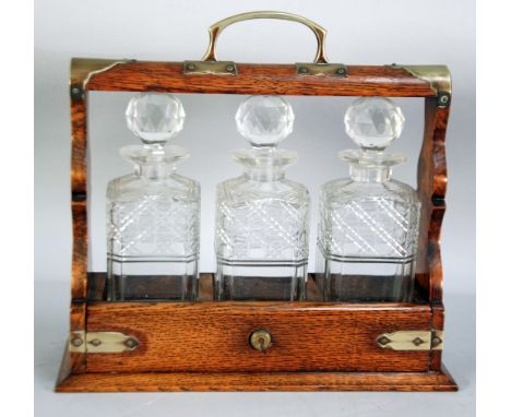 AN EARLY 1900's OAK FRAMED, BRASS MOUNTED THREE CUT GLASS SQUARE DECANTER TANTALUS 