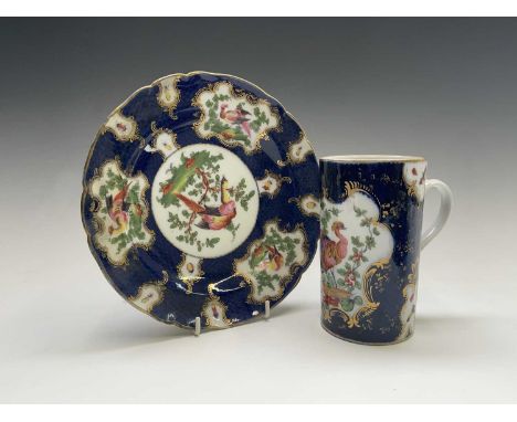 A Continental porcelain mug, in the Worcester style, the blue scale ground with panels of an exotic bird and flowers, height 