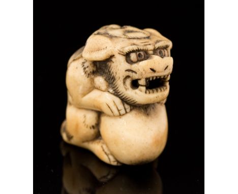 An Oriental bone netsuke, carved as a Foo dog with ball, height 3cm