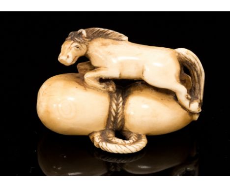 An Oriental ivory netsuke, carved as a horse upon a rope bound sack, signed, width 4cm