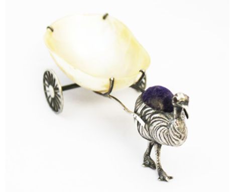 A George V silver figural Emu pin cushion, pulling a mother of pearl pin dish in the form of a cart with two revolving wheels