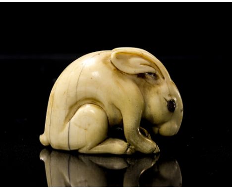 A Japanese carved ivory netsuke, Meiji, modelled as a hare, the eyes inset with orange cabouchons, character seal mark, 5.5cm