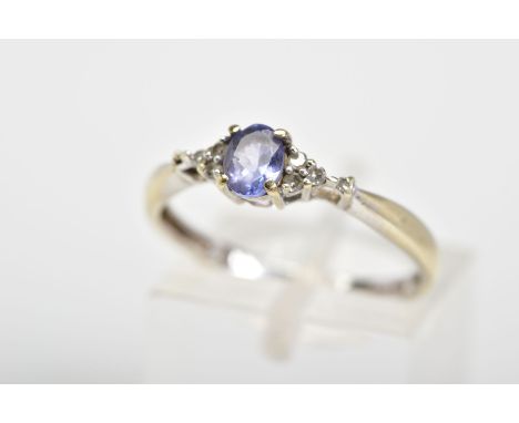 A 9CT WHITE GOLD RING, with a central oval cut tanzanite flanked with colourless stones, to the tapered shoulders, with a 9ct