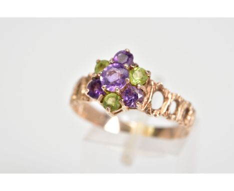 A 9CT GOLD CLUSTER RING, the tiered cluster set with circular cut amethyst and peridot, to the open work textured shoulders, 