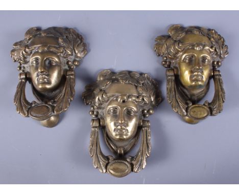 A group of three brass door knockers, in the form of a Roman soldier's head, the knocker cast in the form of a length of acan