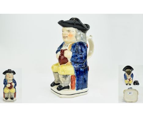 Early 19th Century Period Ralph Wood Type Toby Jug, seated, wearing a black hat, blue coat and yellow trousers, holding a jug