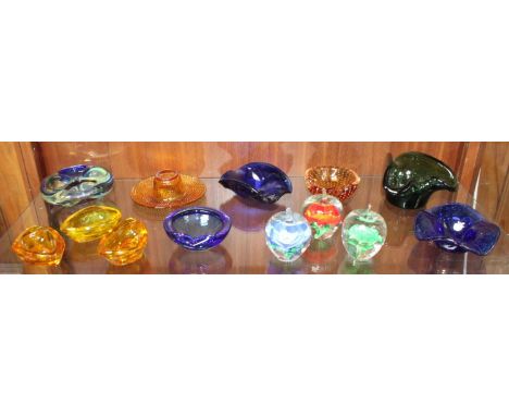 A shelf of coloured glass ashtrays together with three clear glass paperweights modelled as apples with coloured flowers insi