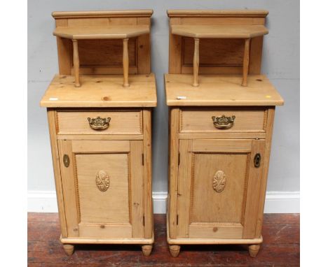 A pair of pine bedside pot cupboards, the raised backs with shelf above a single drawer and carved panel door, raised on turn