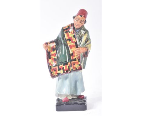 Royal Doulton – Carpet Seller - HN1464 – a hand painted ceramic figure / figurine of a standing carpet seller with carpet dra