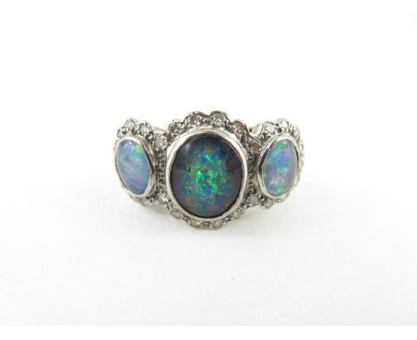 A three stone opal triplet set ring, the white mount stamped ‘18ct’, the graduated stones enclosed by single cut diamonds, th