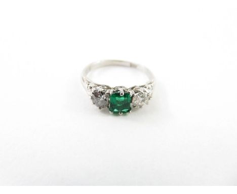 An emerald and diamond three stone ring, the white mount stamped ‘18ct’, the two old brilliant cuts totalling approximately 0