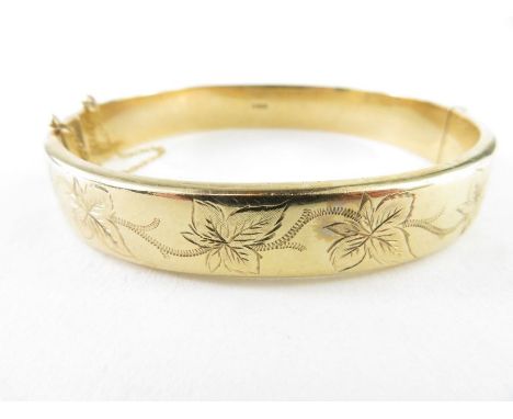 A 9ct gold hinged bangle, with with half engraved decoration of leaves, safety chain, 10.4mm wide, 16.52g gross