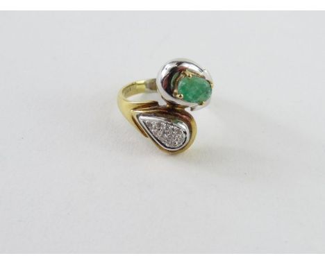 An emerald and diamond cross over dress ring, one side set with a single oval shaped emerald, approximately 6.7mm x 4.8mm, to