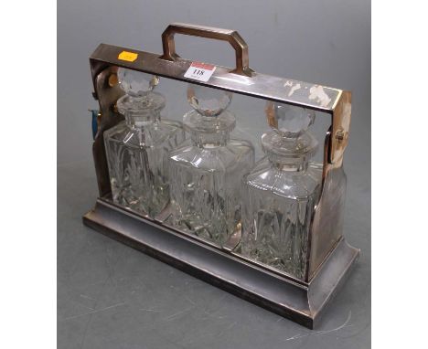 A mid-20th century silver plated three-bottle tantalus, having typical locking stile enclosing three cut glass decanters and 