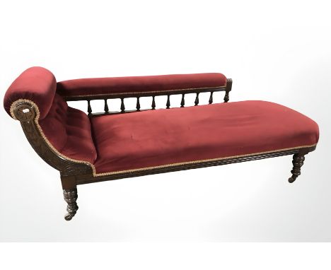 A late Victorian carved oak chaise lounge, in button red upholstery, 185 cm x 65 cm x 75 cm.