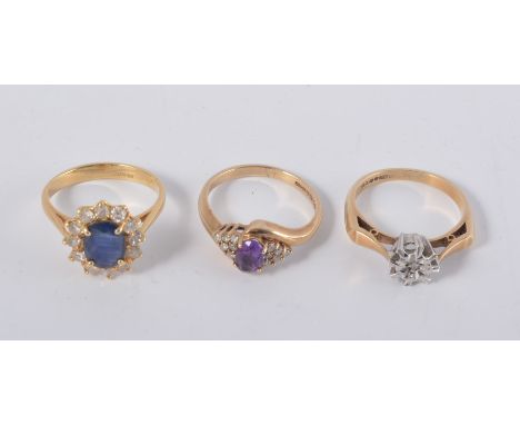 Three dress rings, a sapphire and diamond oval cluster in an all yellow metal mount, an amethyst ring with six small white st