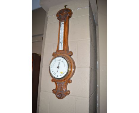 A carved oak banjo shaped barometer, fitted thermometer above the barometer dial and carved with foliate motifs.