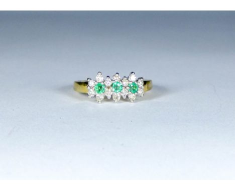 A three stone emerald ring surrounded by diamonds, set in 18ct yellow gold, ring size Q, gross weight approximately 4.46g, 