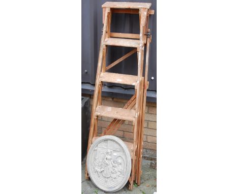 A pine easel decorator's ladder, together with a reconstituted stone Continental oval plaque depicting figures (2)