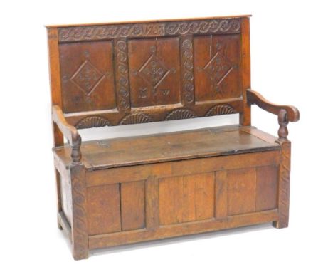 An oak settle, the raised panelled back carved with initials M W and bearing date 1703, the base with a hinged seat and shape