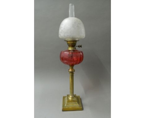 A Victorian oil lamp with cranberry glass reservoir. 76 cm high.