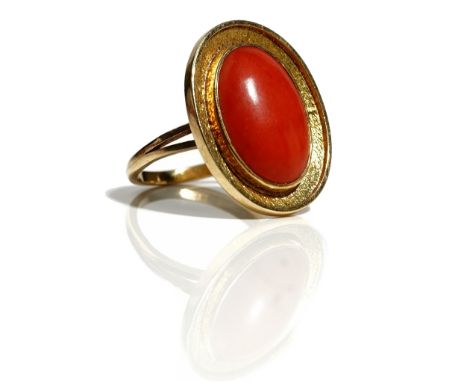 A gold mounted oval coral ring, the oval coral mounted within a textured border, ring size O and a half, unmarked, gross weig