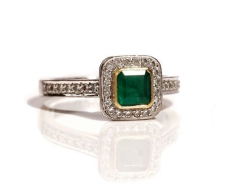 An 18ct white gold, emerald and diamond cluster ring, mounted with the cut cornered square step cut emerald to the centre, in