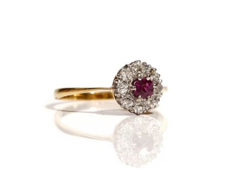 An 18ct gold, ruby and diamond set nine stone cluster ring, claw set with the cushion shaped ruby at the centre, in a surroun