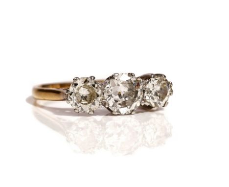 A gold and platinum, diamond set three stone ring, claw set with a row of cushion shaped diamonds and with the principle diam