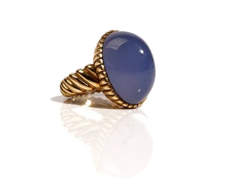 A gold ring, mounted with an oval cabochon blue stained chalcedony, the setting with ridged decoration, the shank with slanti