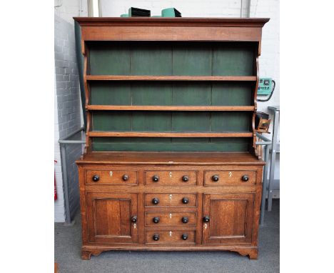A late George III oak dresser, the enclosed three tier plate rack, over six frieze drawers, flanked by cupboards on bracket f
