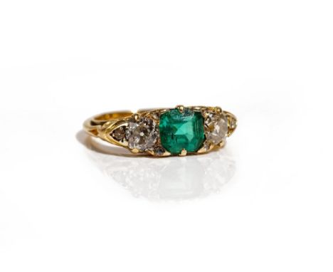 A gold, emerald and diamond ring, mounted with the square step cut emerald to the centre, between the two principal cushion s