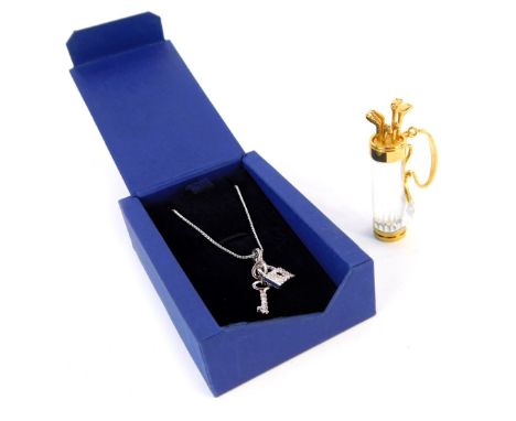 Two Swarovski Crystal items, comprising a golf and caddy brooch, and a heart shaped locket and key pendant, boxed. (2)