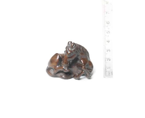 A wood netsuke of a seated horseEarly 19th centuryThe horse lying, turning its head back to lick its right hoof, its forelimb