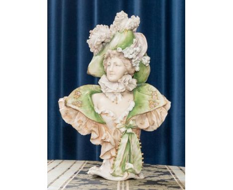 An Austrian (Turn, Teplitz ,Bohemia R St K) porcelain pedestal bust of a lady of fashion circa 1910, wearing a huge feather p