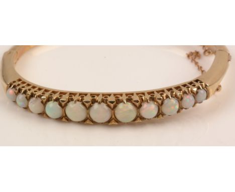 A yellow metal and opal bangle, set with eleven graduated white opal circular cabochons in pierced setting, 6.3cms wide, 23g 