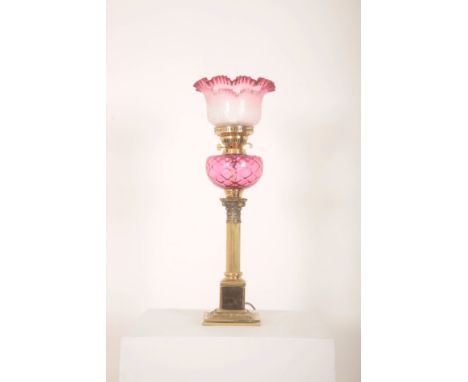 A BRASS TABLE OIL LAMP OF VICTORIAN DESIGNwith spherical cranberry glass reservoir above Corinthian style column, with etched