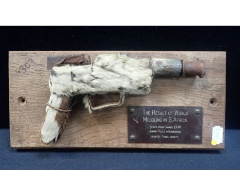 A DUMMY HANDGUN COVERED IN FUR, PROBABLY ZULUand made from scrap metal, mounted on a plaque: 'The result of world meddling in