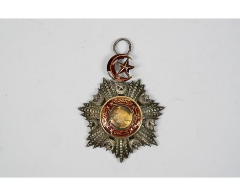 A Turkish Ottoman Order of Medjidie neck badge, the mixed metal badge with red enamel decoration, stamped to reverse