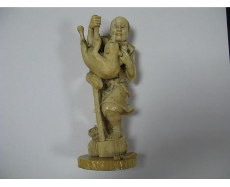 A Late XIX Century Japanese Ivory Figure of a Gentleman Carrying a Wolf, standing on an axe beside a sack on an oval base, 16