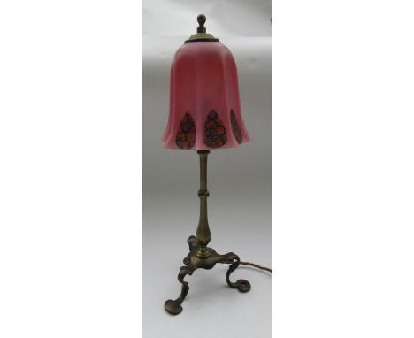 A brass table lamp, in the manner of Benson, on three shaped supports in the Arts and Crafts style, with a pink glass shade, 