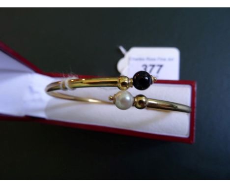 A yellow metal bangle with simulated pearl and black bead terminals.